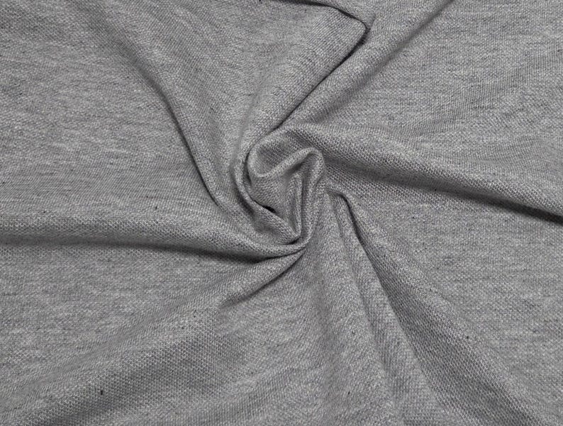 May include: Close-up of gray fabric with a textured surface. The fabric is folded and draped, creating soft shadows and highlights. The material appears to be a medium-weight knit, suitable for apparel or home decor projects.
