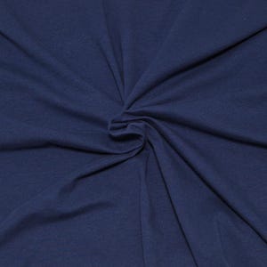 May include: A solid dark navy blue fabric with a smooth, matte texture. The material is gathered in the center, creating soft, radiating folds and natural drapes that extend outward toward the edges of the frame, showcasing the textile's flexibility.