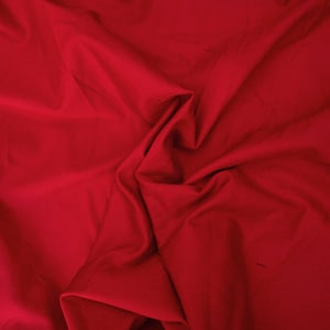 May include: A close-up shot of a vibrant red fabric with soft folds and subtle shadows. The material appears to be smooth and possibly lightweight, with a rich, solid color. The fabric is likely suitable for apparel or home decor.