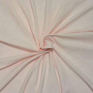 Puede incluir: Una tela de color rosa claro s&oacute;lido con una textura suave, que presenta un remolino central que crea pliegues naturales y l&iacute;neas radiantes en toda la superficie. El material parece suave y flexible, con un color uniforme en toda la pieza.