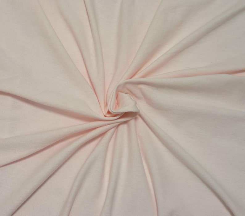 Puede incluir: Una tela de color rosa claro s&oacute;lido con una textura suave, que presenta un remolino central que crea pliegues naturales y l&iacute;neas radiantes en toda la superficie. El material parece suave y flexible, con un color uniforme en toda la pieza.