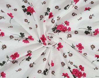 May include: White fabric with a floral pattern. The design features bright pink flowers with green leaves and small brown flowers scattered across the surface. The fabric is folded, creating a textured appearance.