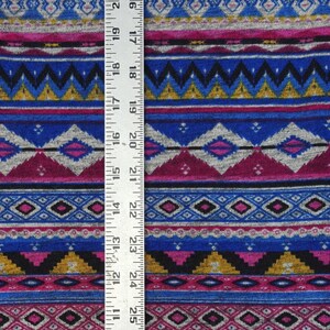 May include: A close-up of a colorful fabric with a geometric pattern. The fabric is a mix of pink, blue, gray, black, and gold. A ruler is placed next to the fabric to show the scale.