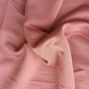 May include: A close-up of a soft, pink fabric with a smooth, silky texture. The fabric is draped and folded, creating a sense of movement and flow.