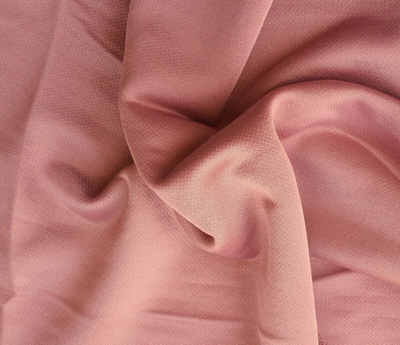 May include: A close-up of a soft, pink fabric with a smooth, silky texture. The fabric is draped and folded, creating a sense of movement and flow.