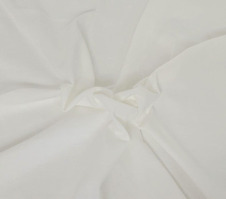 Puede incluir: Una tela blanca s&oacute;lida con una textura suave y mate, que presenta pliegues suaves y drapeados delicados que crean sombras sutiles en la superficie. El material parece ligero y opaco, con un color blanco constante, limpio y neutro en todo el conjunto.