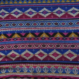 May include: A close-up of a fabric with a colorful geometric pattern. The pattern features a repeating design of diamonds, triangles, and stripes in shades of blue, pink, gold, and black.