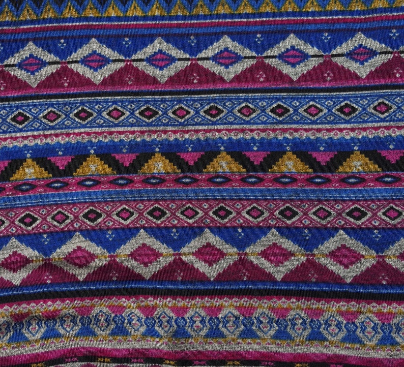 May include: A close-up of a fabric with a colorful geometric pattern. The pattern features a repeating design of diamonds, triangles, and stripes in shades of blue, pink, gold, and black.