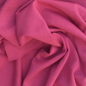 May include: Close-up of a soft, pink fabric with a ribbed texture. The fabric is folded and draped, showing its smooth and flowing quality.