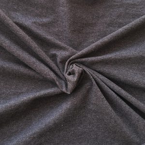 Puede incluir: Una tela de color gris carb&oacute;n oscuro con una textura jaspeada y una apariencia de tejido suave. El material est&aacute; recogido en el centro, creando pliegues y drapeados naturales que resaltan las sutiles variaciones en los tonos de gris oscuro.
