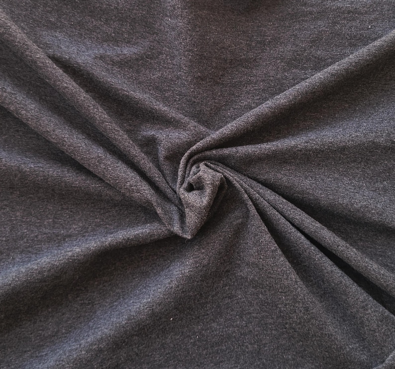 Puede incluir: Una tela de color gris carb&oacute;n oscuro con una textura jaspeada y una apariencia de tejido suave. El material est&aacute; recogido en el centro, creando pliegues y drapeados naturales que resaltan las sutiles variaciones en los tonos de gris oscuro.