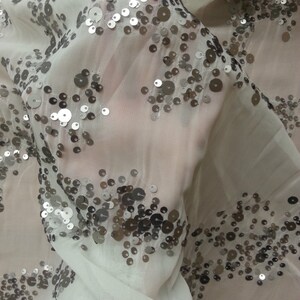 May include: White sheer fabric with silver sequins scattered across the surface. The sequins are arranged in a random pattern.