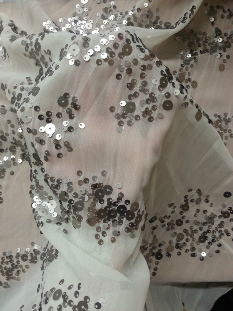 May include: White sheer fabric with silver sequins scattered across the surface. The sequins are arranged in a random pattern.