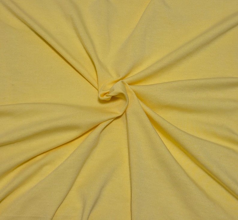 May include: A solid light yellow fabric with a smooth, matte texture. The material is gathered in the center, creating soft, radiating folds and natural drapes that extend outward toward the edges of the frame, highlighting the consistent color.