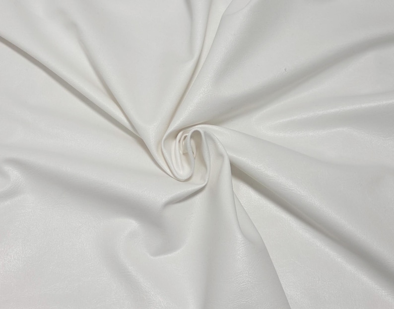 Pode incluir: Close-up de tecido branco com uma superf&iacute;cie lisa e ligeiramente texturizada. O material &eacute; dobrado e drapeado, criando sombras suaves e destaques. O tecido parece ser um material sint&eacute;tico, possivelmente couro sint&eacute;tico ou um t&ecirc;xtil semelhante.