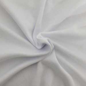 May include: A solid white fabric featuring a distinct vertical ribbed texture. The material is gathered in the center, creating soft, flowing folds and shadows that highlight the consistent linear pattern across the surface of the textile.