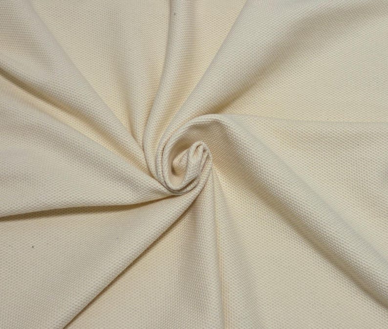 May include: Cream-colored fabric with a textured, woven pattern. The fabric is arranged in soft folds, with a central swirl. The material appears to be thick and durable, suitable for upholstery or clothing.