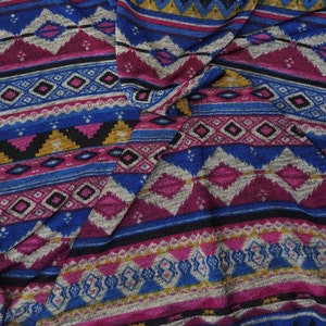 May include: A close-up of a fabric with a colorful geometric pattern. The pattern features shades of blue, pink, gold, and black. The fabric is woven with a textured surface.