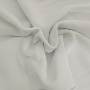 May include: A close-up of a white fabric with a smooth, textured surface. The fabric is folded and draped, creating soft folds and curves.