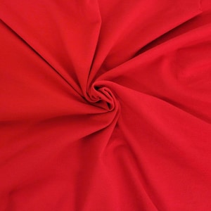 May include: A vibrant red fabric with a smooth, matte texture, displayed with deep, flowing folds that radiate from a central point, creating a series of soft, natural shadows and highlights across the surface of the solid-colored textile material.