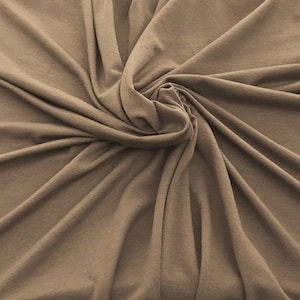 May include: A close-up of a brown fabric with a soft, wrinkled texture. The fabric is folded and draped in a way that creates a swirling pattern.