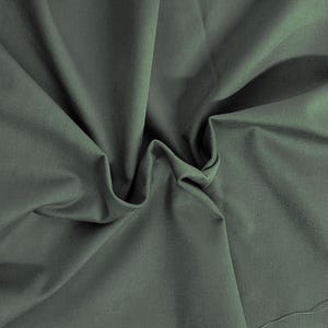 May include: A close-up of a soft, green fabric with a smooth texture. The fabric is folded and draped, creating a sense of movement and flow.