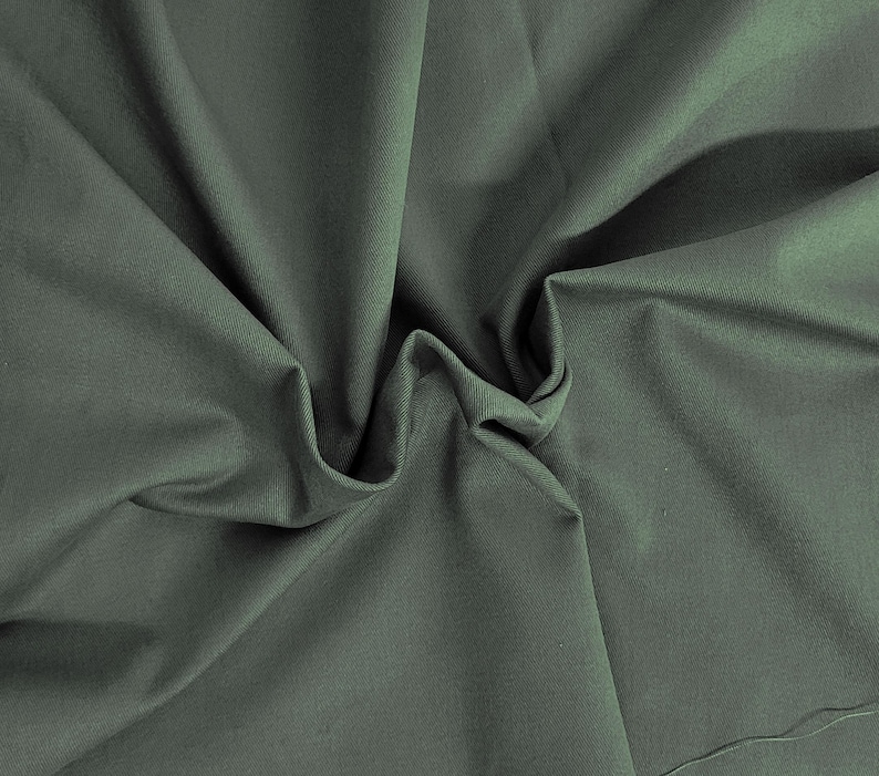 May include: A close-up of a soft, green fabric with a smooth texture. The fabric is folded and draped, creating a sense of movement and flow.