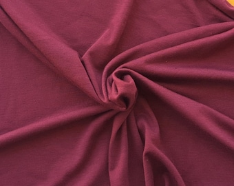 May include: A close-up of a deep burgundy fabric with a soft, smooth texture. The fabric is draped and folded, creating a sense of movement and flow.