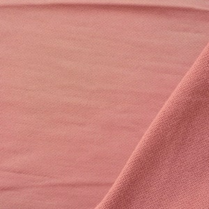 May include: A close-up of a soft, pink fabric with a textured surface. The fabric is folded in half, creating a diagonal line across the image.