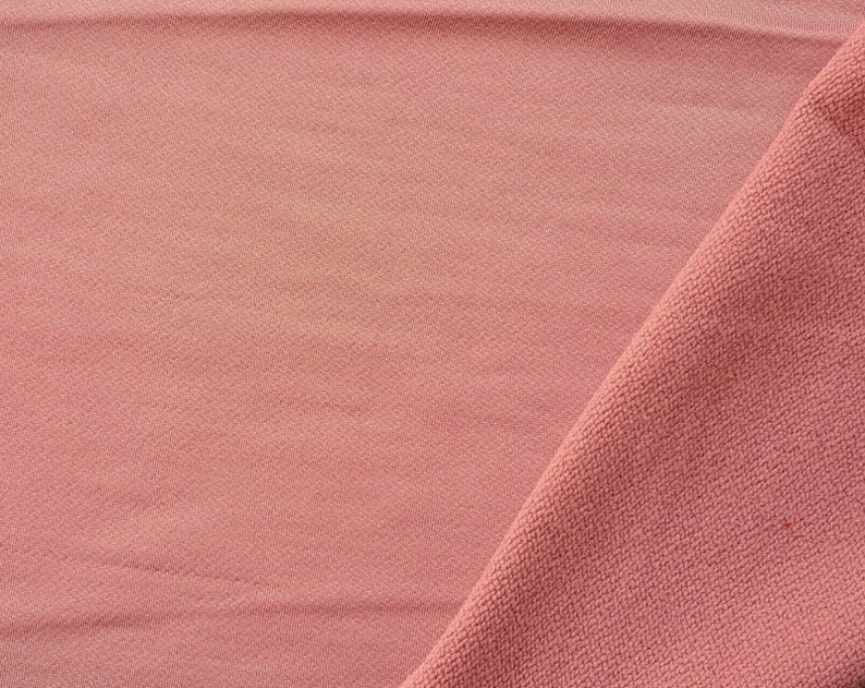 May include: A close-up of a soft, pink fabric with a textured surface. The fabric is folded in half, creating a diagonal line across the image.
