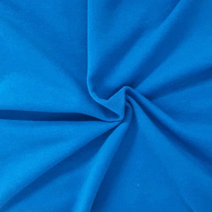 May include: A close-up shot of a vibrant, solid blue fabric. The material is soft and appears to be draped, with subtle folds and shadows adding depth. The color is a bright, saturated blue, filling the frame.