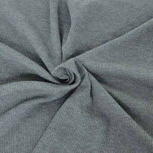 May include: Close-up of a textured, gray fabric with a woven pattern. The fabric is folded and swirled, creating a spiral effect in the center. The material appears soft and pliable, suitable for clothing or home decor.