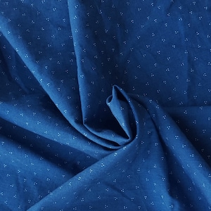 May include: A close-up of a blue fabric with a white polka dot pattern. The fabric is folded and textured, showing the depth of the material.