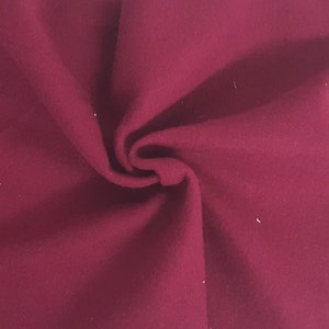 May include: Close-up of a deep burgundy fabric with a soft, textured appearance. The material is folded, creating shadows and highlighting the fabric's depth and color. The fabric appears to be a solid color, with no visible patterns or designs.