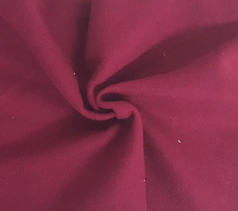May include: Close-up of a deep burgundy fabric with a soft, textured appearance. The material is folded, creating shadows and highlighting the fabric's depth and color. The fabric appears to be a solid color, with no visible patterns or designs.