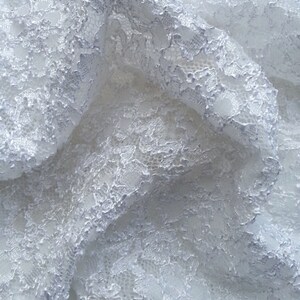 May include: White lace fabric with a delicate floral pattern. The lace is soft and flowing, with a slightly textured surface.