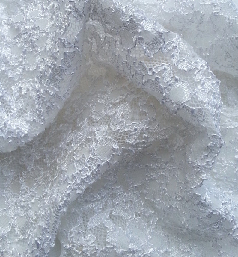 May include: White lace fabric with a delicate floral pattern. The lace is soft and flowing, with a slightly textured surface.