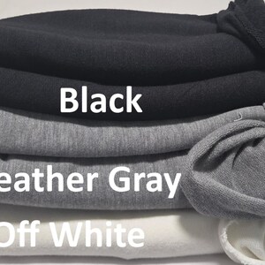 May include: A stack of three folded garments in black, heather gray, and off-white. The text Black is printed on the black garment, Heather Gray is printed on the gray garment, and Off White is printed on the off-white garment.