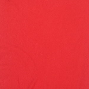 May include: Solid red fabric with a smooth texture. The fabric is slightly wrinkled.