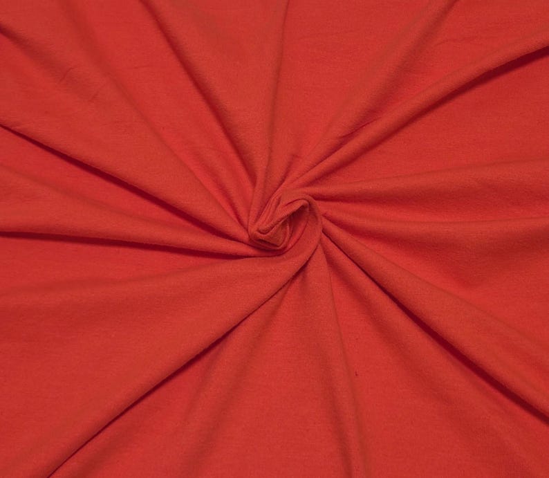 May include: A solid, vibrant red fabric featuring a soft, matte texture. The material is gathered in the center, creating natural, radiating folds and deep shadows that highlight the consistent, bold color across the entire surface of the textile.