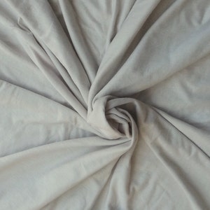 May include: A close-up of a light gray fabric with a soft, smooth texture. The fabric is draped and folded, creating a flowing, elegant look.