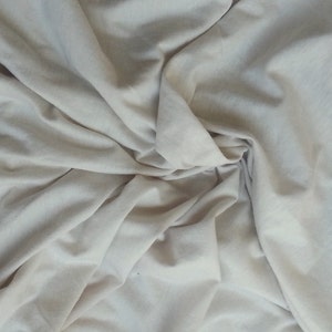 May include: A close-up of a white fabric with soft folds and wrinkles. The fabric is smooth and has a subtle sheen.