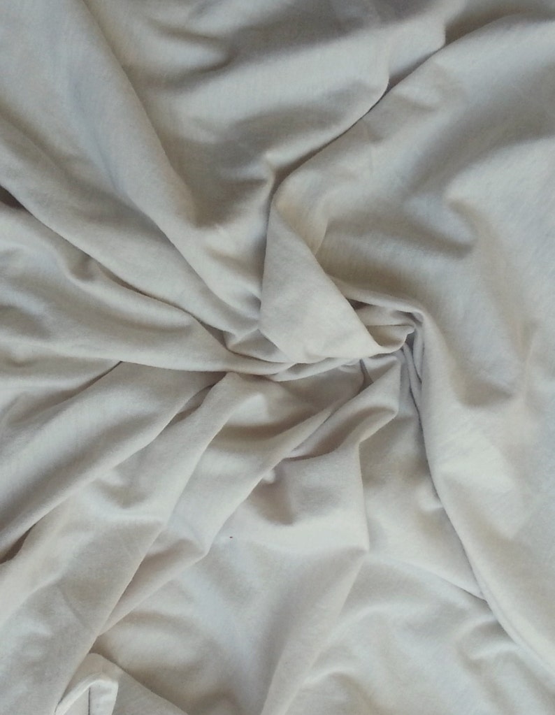 May include: A close-up of a white fabric with soft folds and wrinkles. The fabric is smooth and has a subtle sheen.