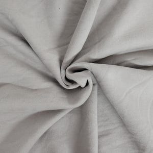 May include: A light gray fabric with a soft, matte texture, featuring deep, flowing folds and natural drapes that create a series of shadows and highlights across the surface, emphasizing the smooth, consistent color and pliable nature of the material.
