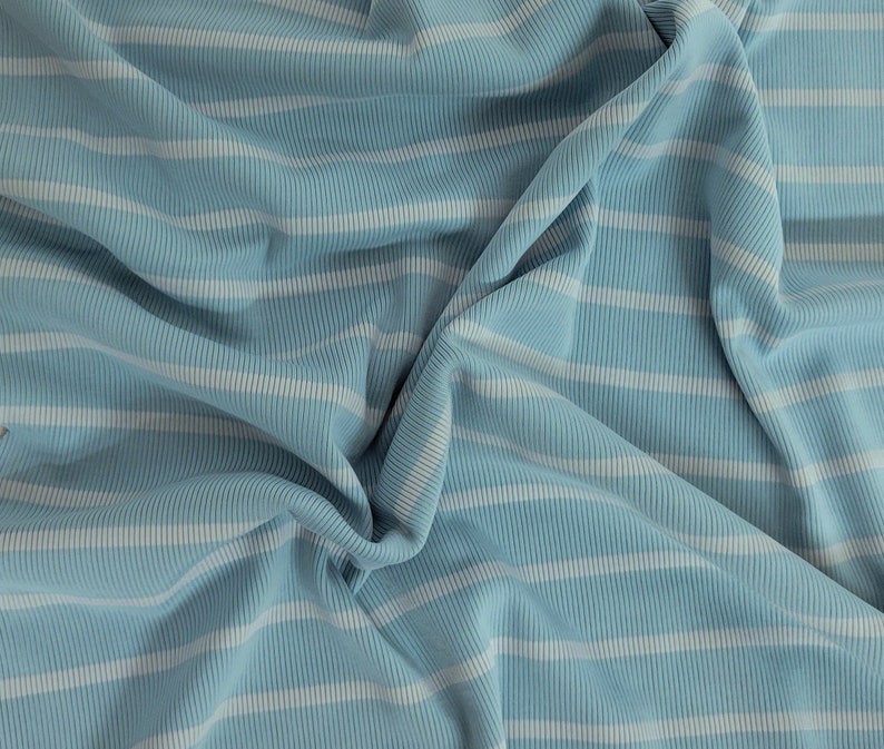 May include: A close-up of a blue and white striped fabric with a ribbed texture. The fabric is folded and creased, creating a soft and inviting look.