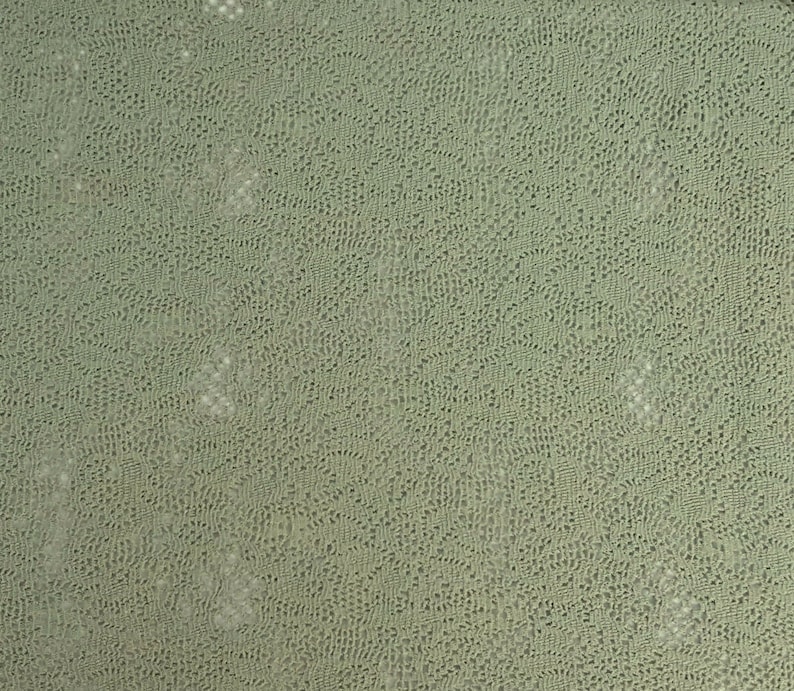 May include: A close-up of a light green textured fabric with a subtle pattern. The fabric has a slightly rough texture and a soft, muted color.