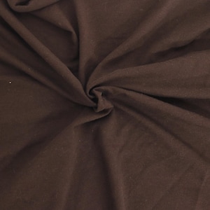 May include: A solid dark brown fabric with a soft, matte texture. The material is gathered in the center, creating natural folds and drapes that radiate outward, showcasing the consistent deep brown color and the smooth, opaque surface of the textile.