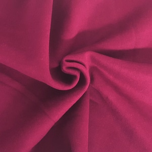 May include: A solid magenta fabric with a smooth, matte texture. The material is gathered in the center, creating soft, flowing folds and deep shadows that highlight the consistent, vibrant pinkish-red color across the entire surface.