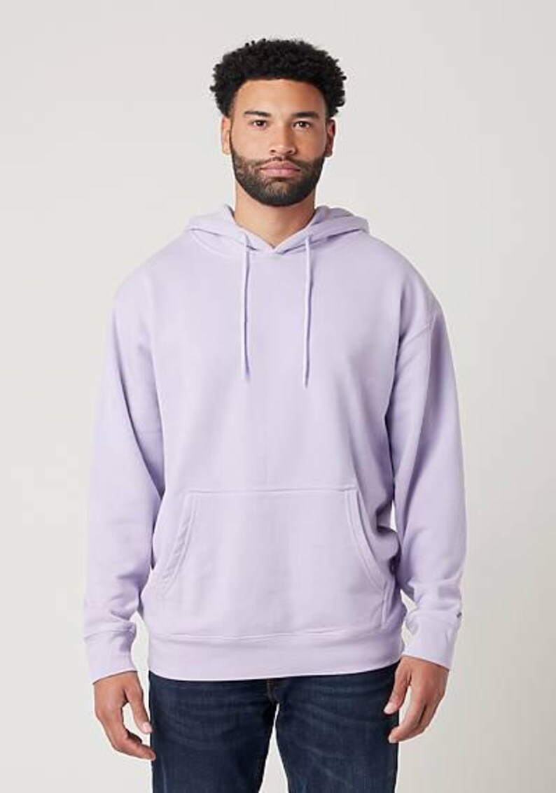 May include: A light purple hoodie with a front pocket and a drawstring hood. The hoodie is made of a soft material and is worn with blue jeans. The model is standing in front of a white background.
