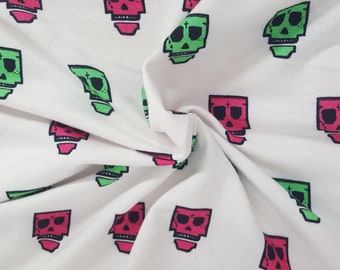 May include: White fabric with a repeating pattern of stylized skulls. The skulls are in shades of green and pink, with black outlines and cross details. The fabric is slightly wrinkled, showing the texture.